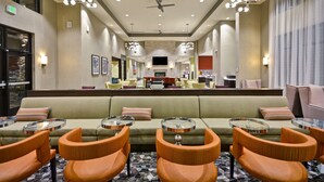 A hotel lobby with a central seating area, multiple tables, and a large television screen.