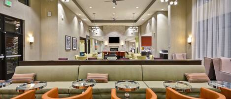 A hotel lobby with a central seating area, multiple tables, and a large television screen.