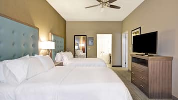 A hotel room with two beds, a ceiling fan, a television, and a dresser.