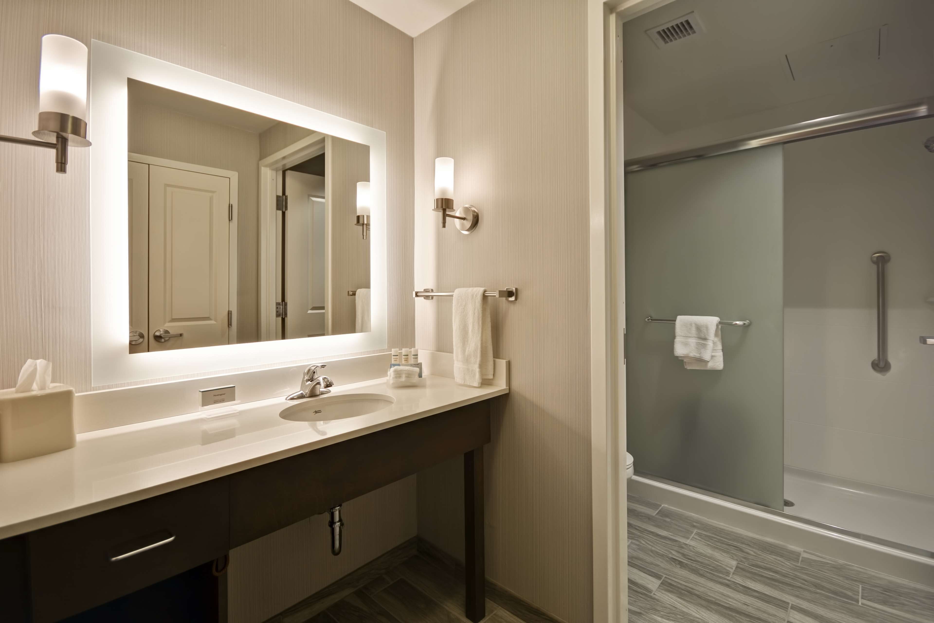 A modern bathroom with a large mirror, a sink, and a glass-enclosed shower.