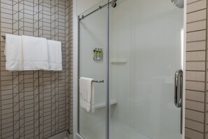 A glass-enclosed shower with a white towel rack and a small shelf with toiletries. - Holiday Inn Express & Suites Gainesville - Lake Lanier Area by IHG (Gainesville)