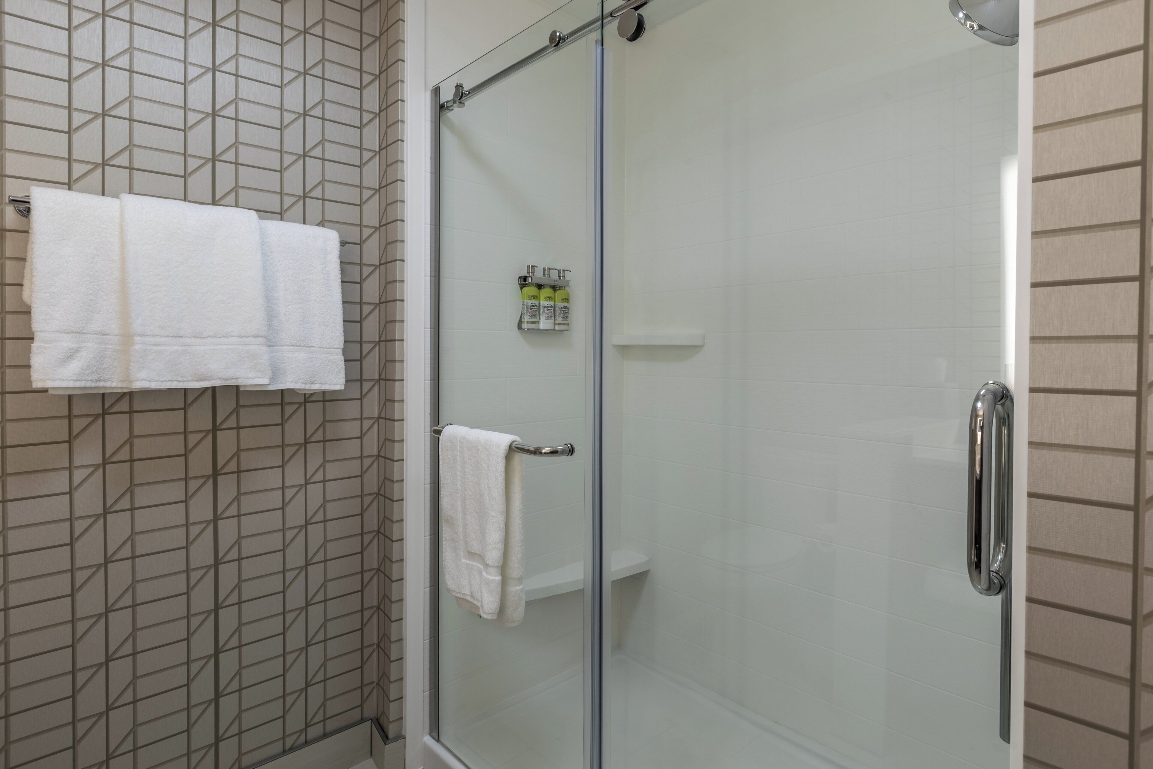 A glass-enclosed shower with a white towel rack and a small shelf with toiletries.