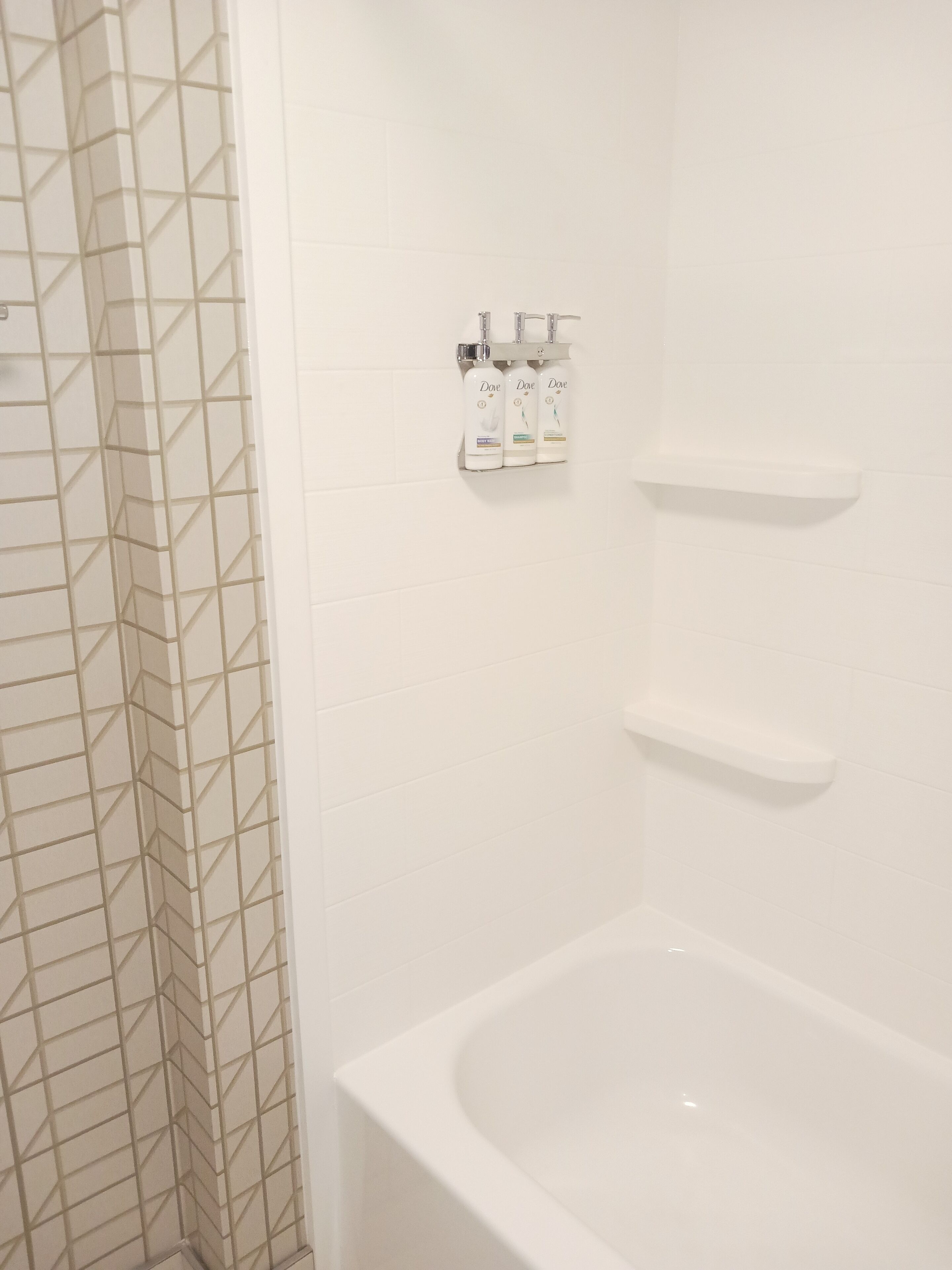 Un baño con una bañera blanca, una zona de ducha con un diseño de baldosas geométricas y un estante con artículos de aseo.