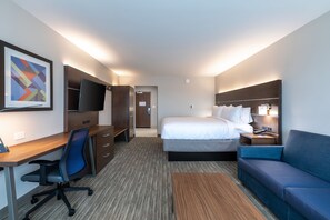 A hotel room with a bed, a desk with a chair, a TV, a sofa, and a framed picture on the wall. - Holiday Inn Express & Suites Gainesville - Lake Lanier Area by IHG (Gainesville)