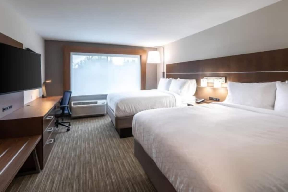 A hotel room with two beds, a desk, a chair, a TV, and a large window.