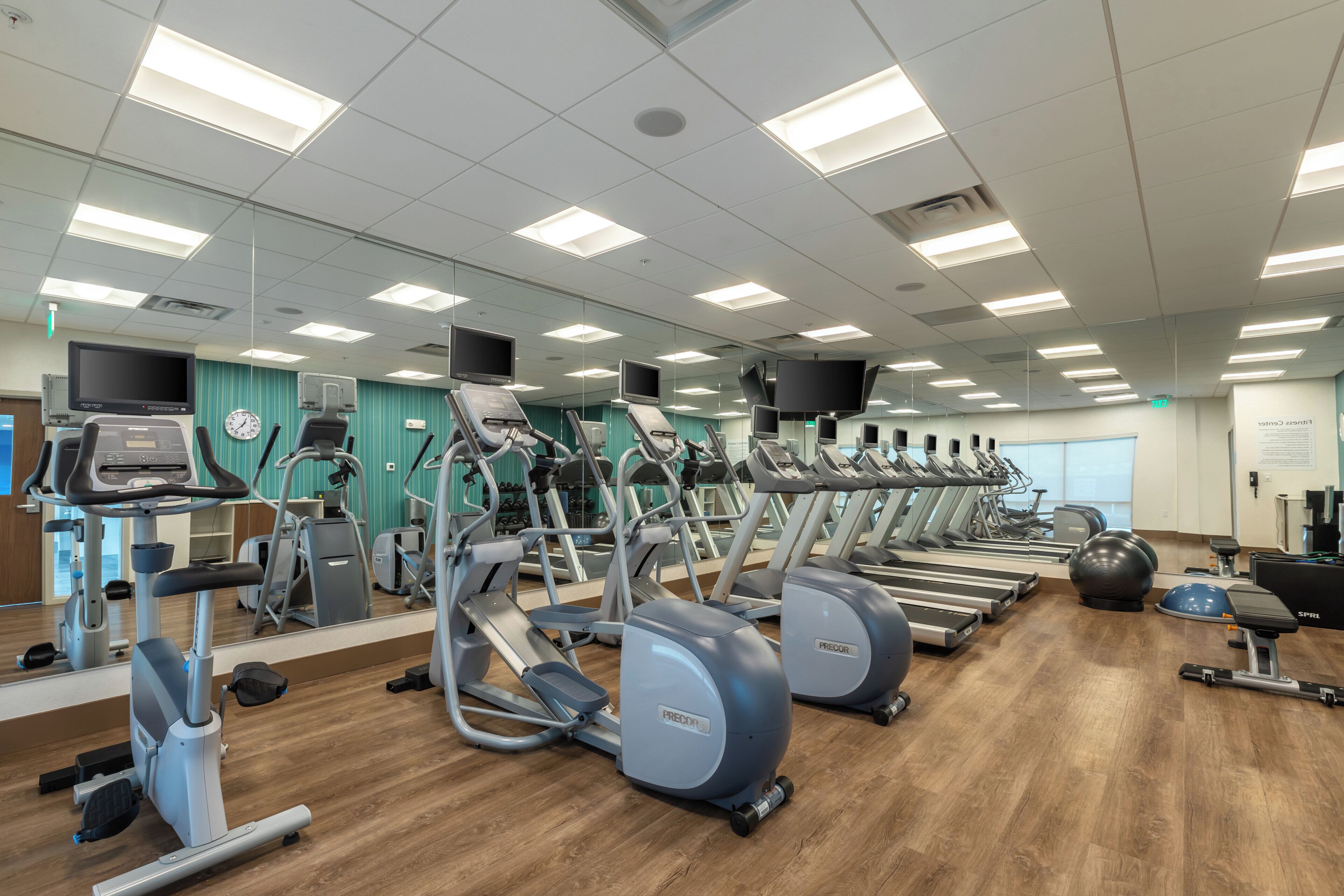 Un gimnasio con numerosas cintas de correr, elípticas y pelotas de ejercicios.