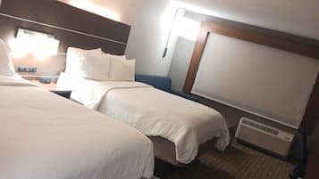 A hotel room with two beds, a nightstand, a lamp, a heater, and a wooden headboard.