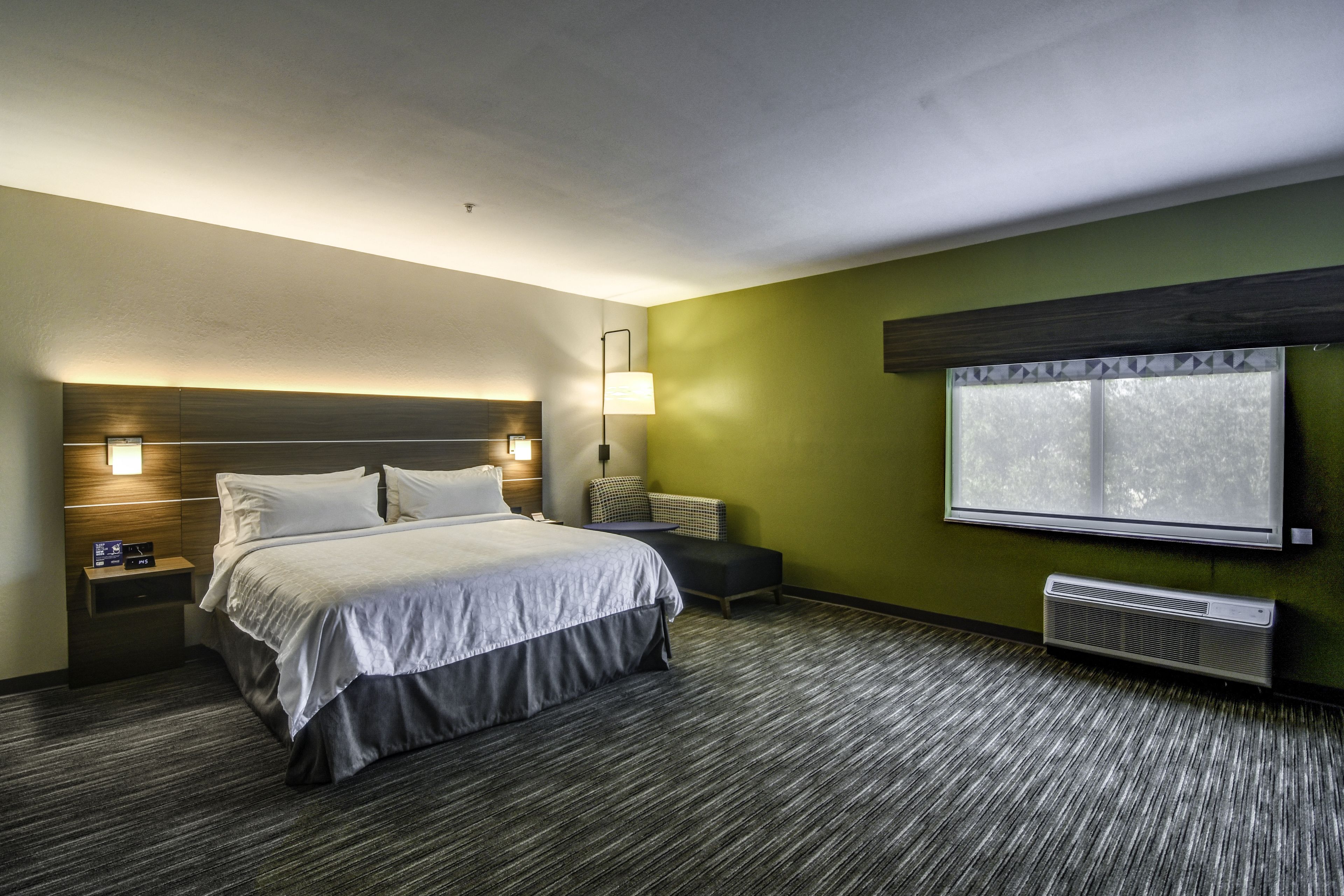 Habitación de hotel con cama, mesitas de noche, lámpara, ventana y aire acondicionado.