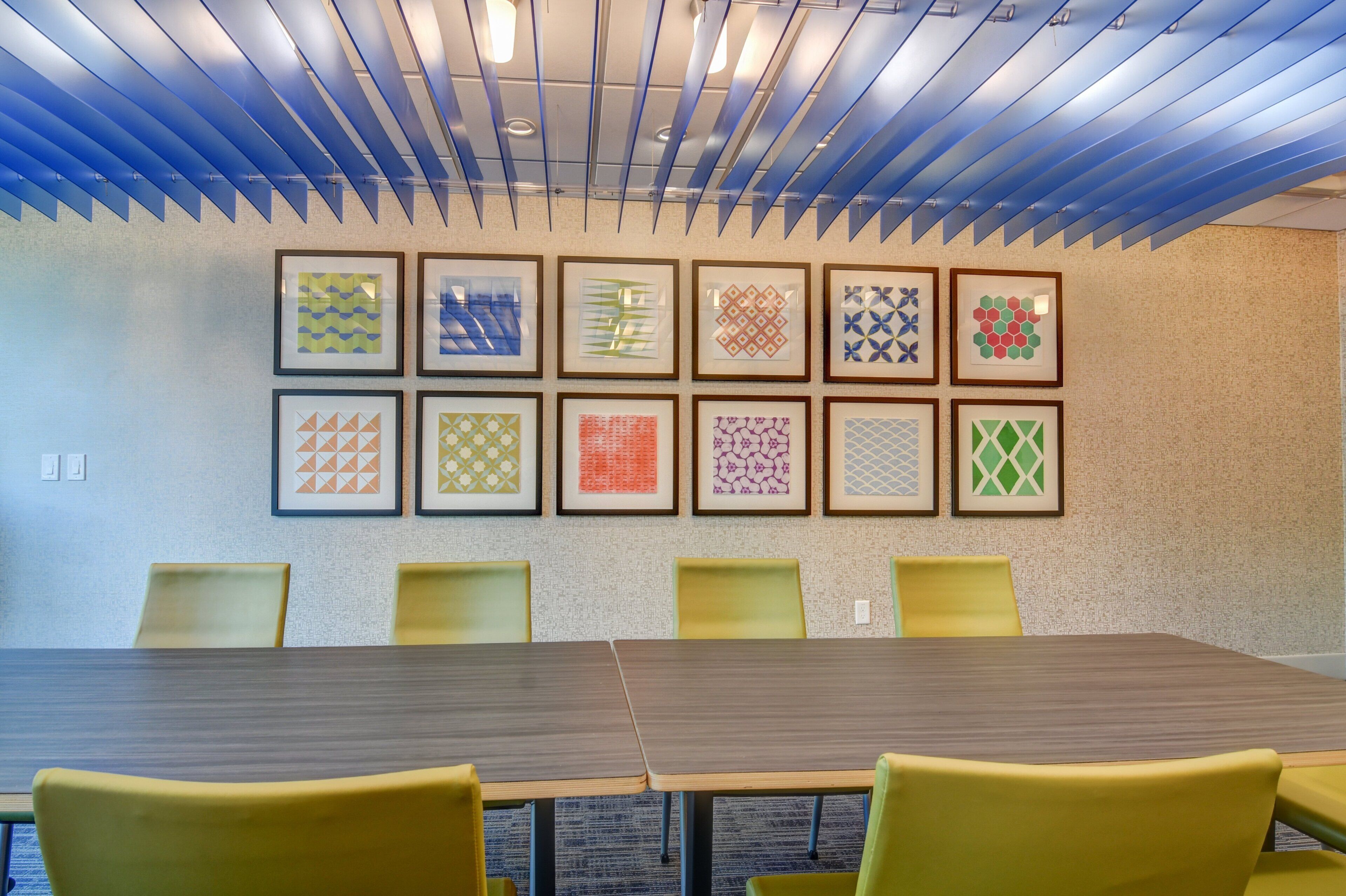 A conference room with a long table and yellow chairs, decorated with framed geometric patterns on the wall.