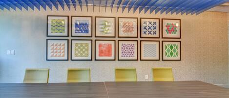 A conference room with a long table and yellow chairs, decorated with framed geometric patterns on the wall.