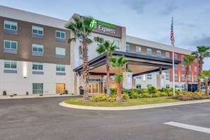 A Holiday Inn Express hotel with a modern facade, multiple windows, and a landscaped entrance area with palm trees and plants. - Holiday Inn Express Fort Walton Beach Central by IHG (Fort Walton Beach)
