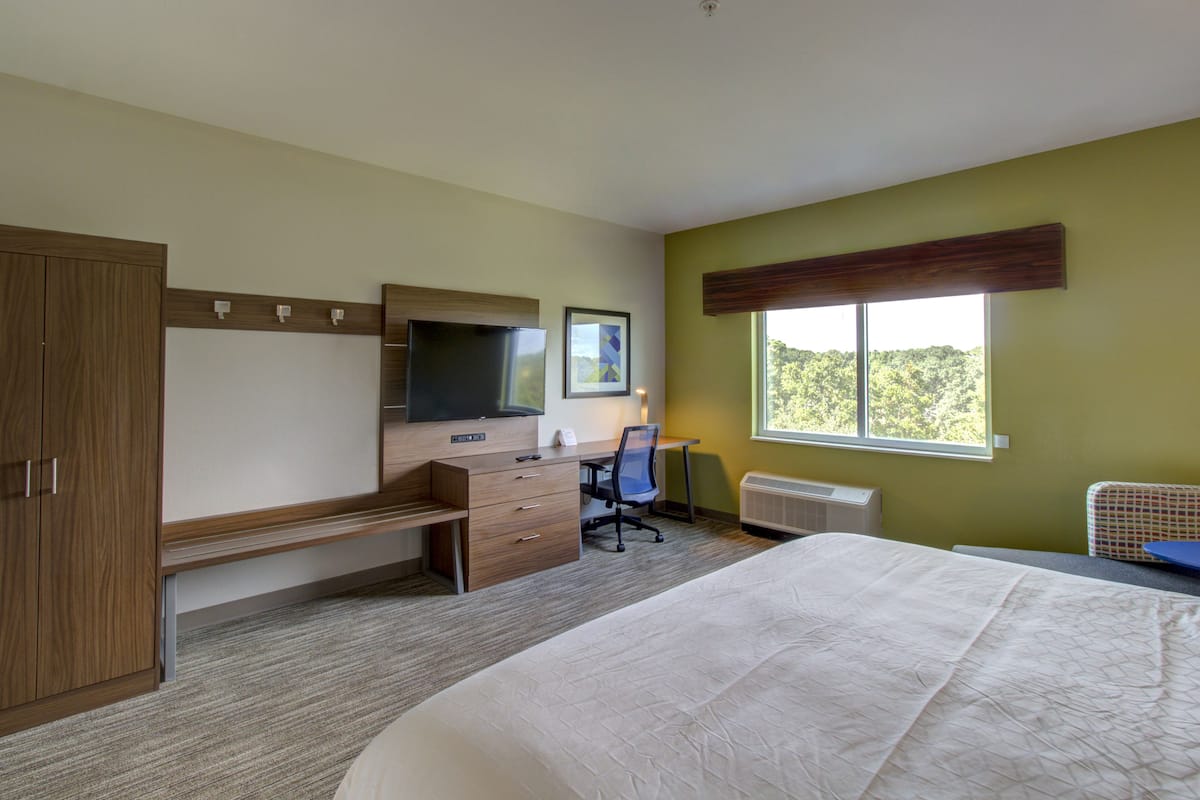A hotel room with a bed, a desk, a chair, a television, and a window with a view of trees.