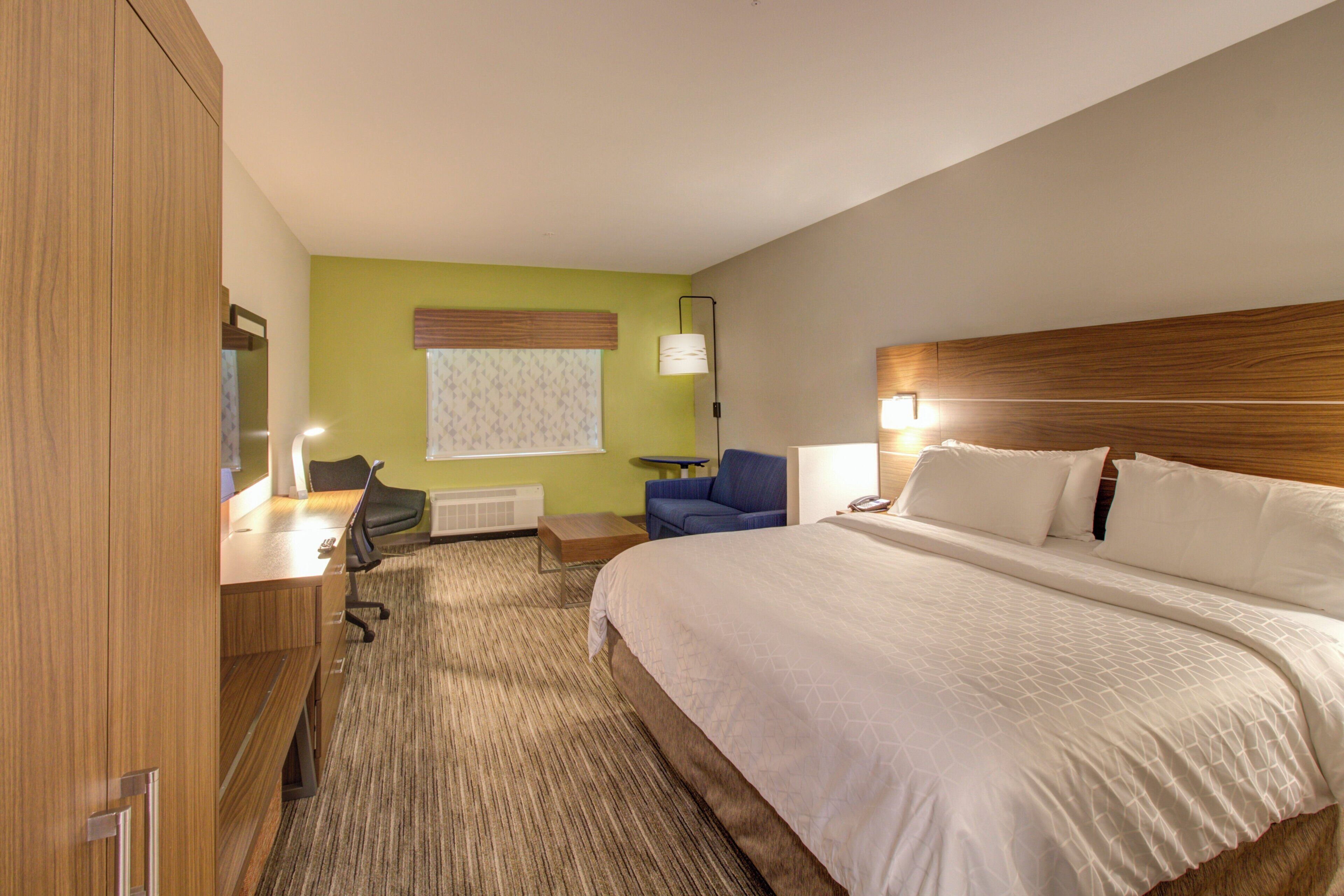 A hotel room with a bed, a desk, a chair, a lamp, and a window with blinds.