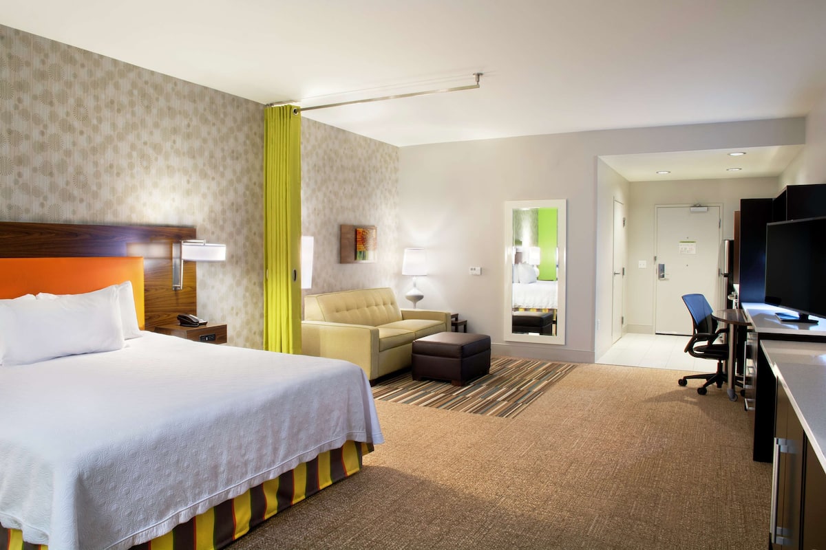Une chambre d’hôtel avec un grand lit, un canapé, un bureau avec un ordinateur et une télévision.