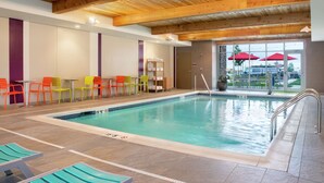 An indoor swimming pool with colorful chairs, a wooden ceiling, and a view of the outside area with umbrellas.