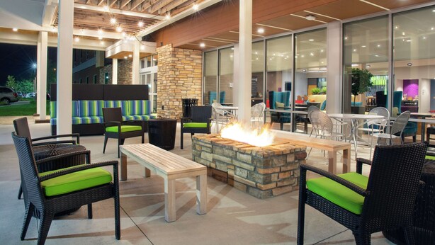 An outdoor patio area with wicker furniture, a stone fire pit, and glass walls overlooking the interior.
