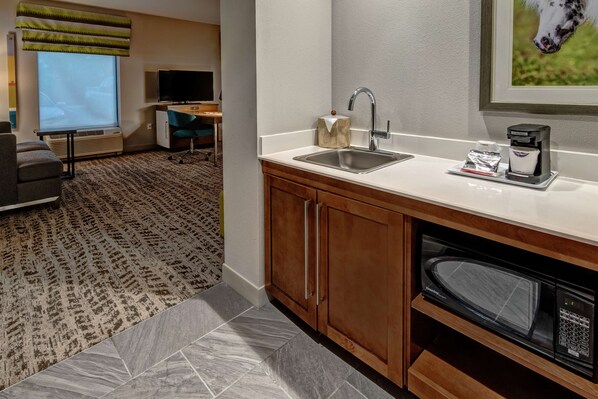 A hotel room with a kitchenette, including a sink, microwave, and coffee maker.