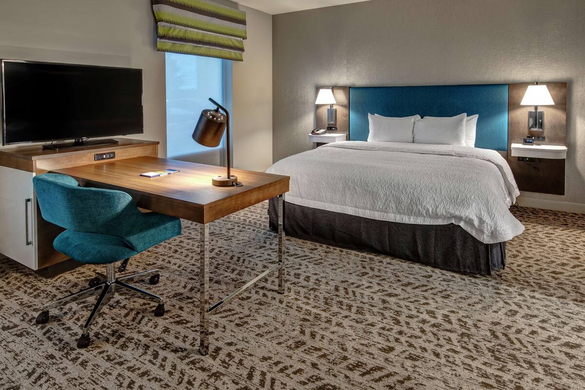 Een hotelkamer met een bed, een bureau met een televisie, een stoel en twee bedlampen.