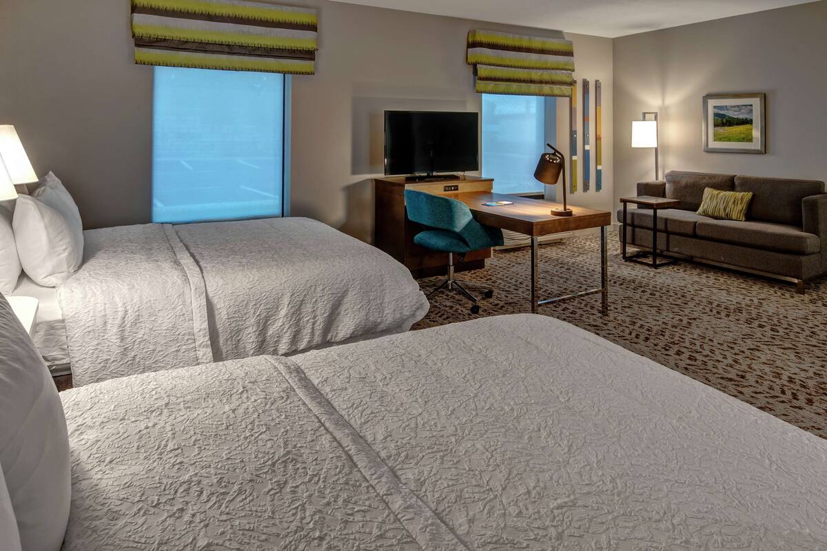 Een hotelkamer met twee bedden, een bureau met stoel, een televisie, een bank en een lamp.