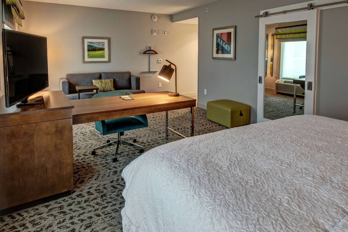 Hotelkamer met een groot bed, een bureau met een lamp, een bank, een televisie en een schilderij aan de muur.