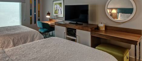 Habitación de hotel con dos camas, un escritorio con televisor, una silla, un espejo y una ventana con cortina.