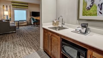 A hotel room with a kitchenette, a sofa, a desk, and a large window.