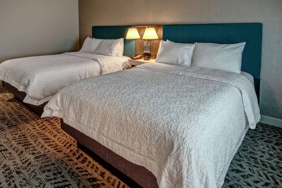 Een hotelkamer met twee bedden, een hoofdeinde, een nachtkastje met een lamp en een kamerbreed tapijt met dessin.