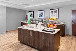 A modern hotel breakfast area with a wooden counter, various food items, and framed pictures on the wall.
