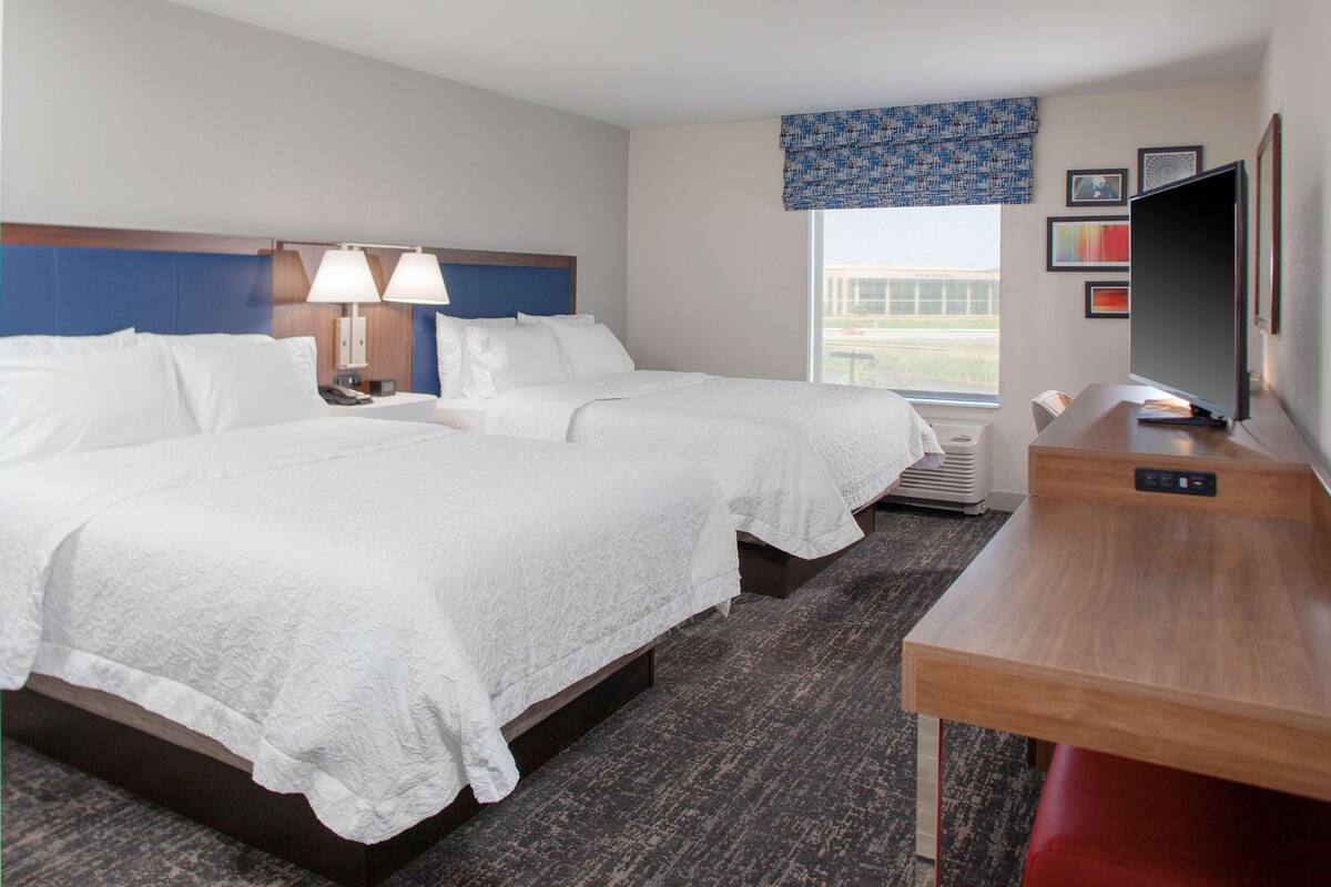 A hotel room with two beds, a desk, a television, and a window with a view.