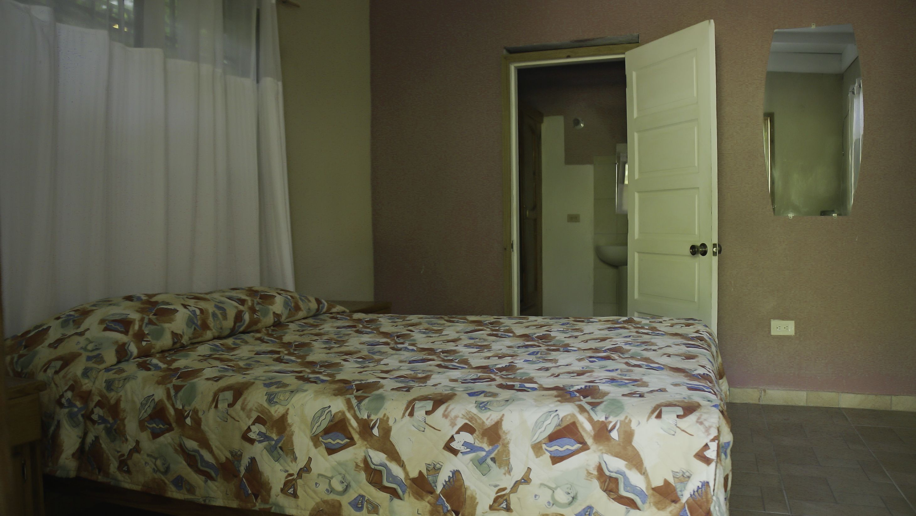 A bedroom with a bed, a door, and a mirror on the wall.