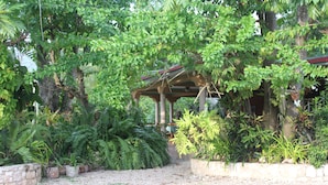 A covered outdoor area with a gravel path, surrounded by various potted plants and trees. - Le Jardin Hotel Restaurant (Jacmel)
