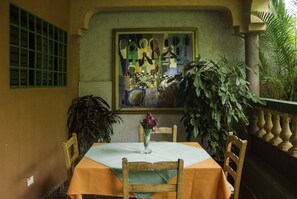 A dining area with a table set for two, a vase with flowers, and a painting on the wall. - Le Jardin Hotel Restaurant (Jacmel)