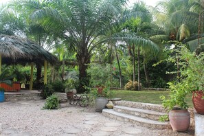 A tropical garden with palm trees, a thatched-roof structure, and stone steps leading to a seating area.