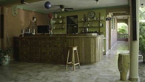 A bar area with a patterned counter, stools, and a ceiling fan. - Le Jardin Hotel Restaurant (Jacmel)