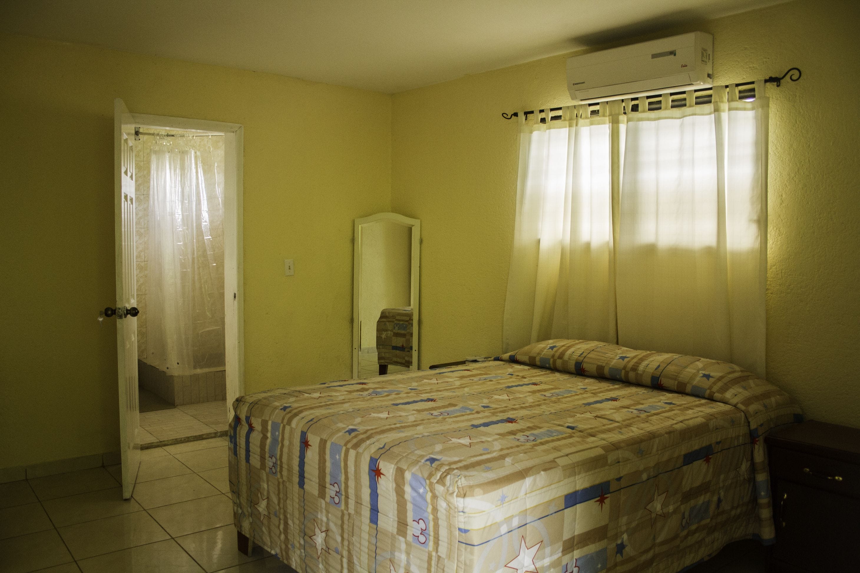 Un dormitorio con una cama, una puerta que da a un baño y un equipo de aire acondicionado en la pared.