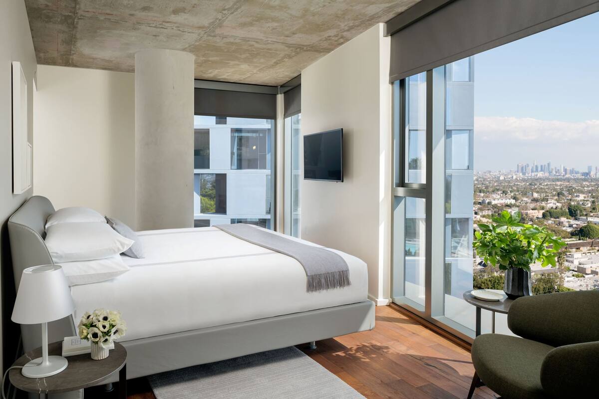 A modern bedroom with a large bed, a TV, and a view of a cityscape.