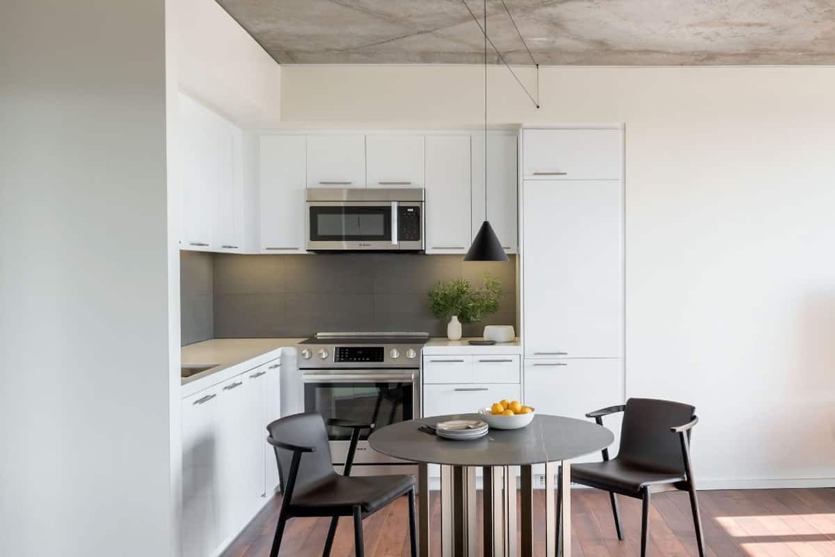 A modern kitchen with white cabinets, a built-in microwave, and a dining area with a round table and two chairs.