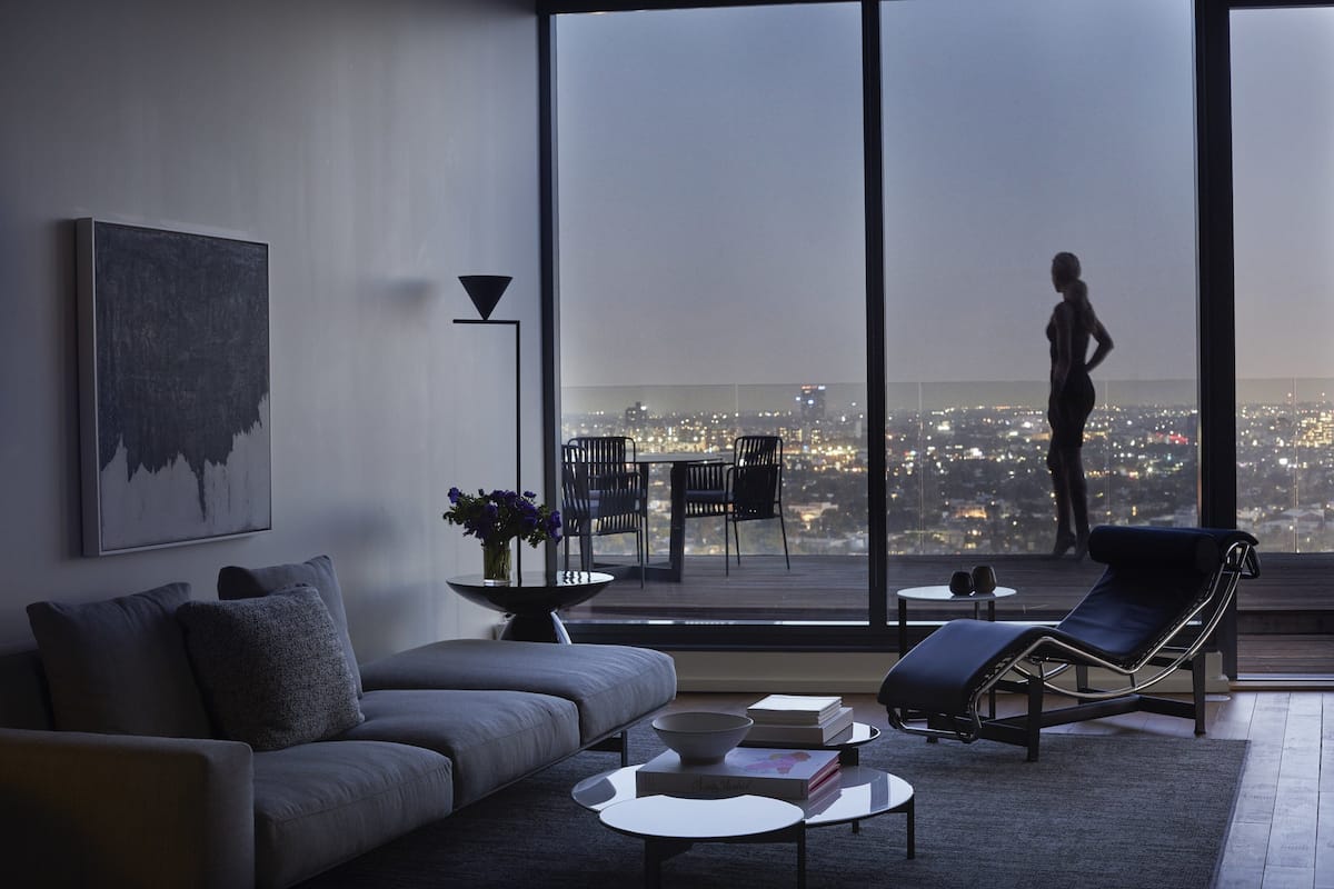 A modern living room with a sofa, a lounge chair, a coffee table, and a view of a cityscape through large windows.