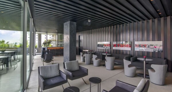 A modern outdoor seating area with contemporary furniture, a bar, and large windows offering views of the city.