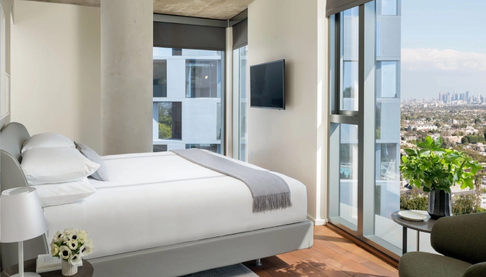 Ein modernes Schlafzimmer mit einem großen Bett, einem Fernseher und Blick auf die Stadt.