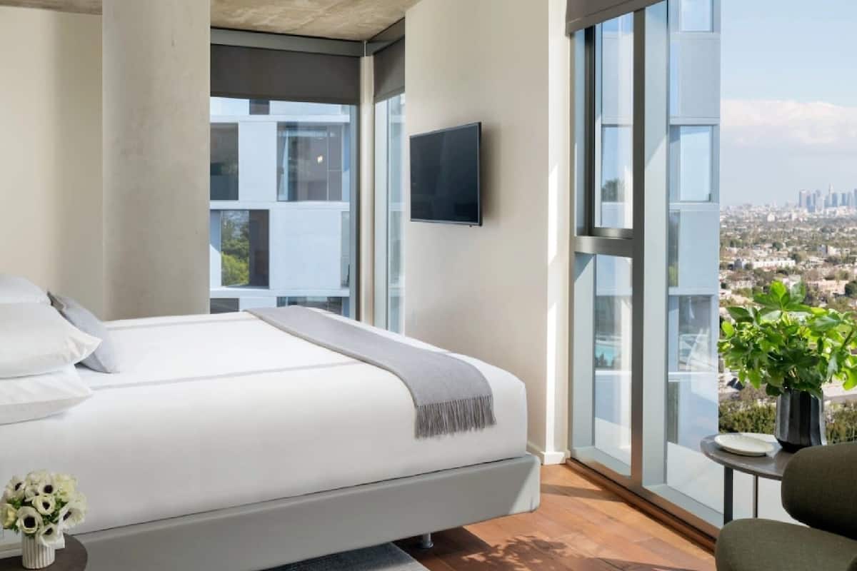 A modern bedroom with a large bed, a TV, and a city view.