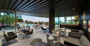 A modern outdoor lounge area with seating, a pool, and a view of the city skyline.