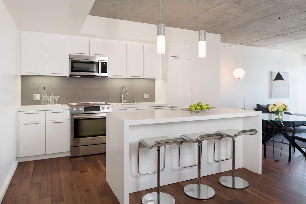 A modern kitchen with white cabinetry, stainless steel appliances, and a central island with bar stools.