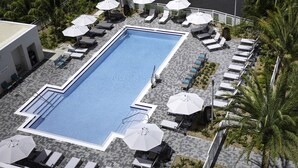A rectangular pool with lounge chairs and umbrellas, surrounded by palm trees and a paved deck. - EVEN Hotel Miami - Airport by IHG (Miami)