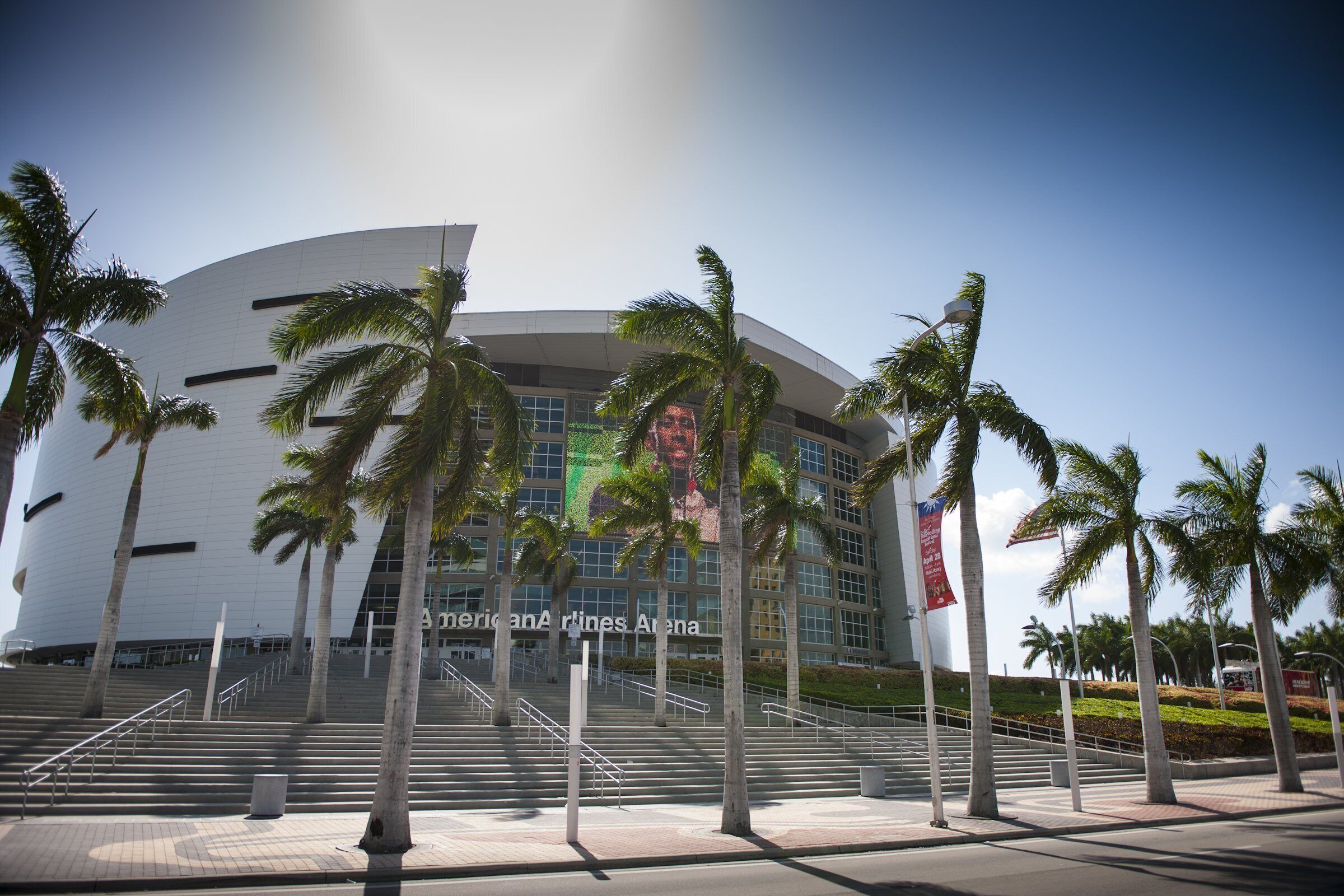 A modern building with a curved facade, palm trees, and a large digital billboard.
