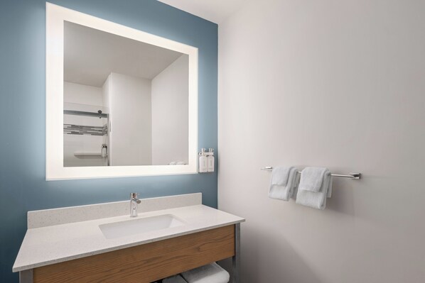 Une salle de bain avec un lavabo blanc, un grand miroir et un porte-serviettes.