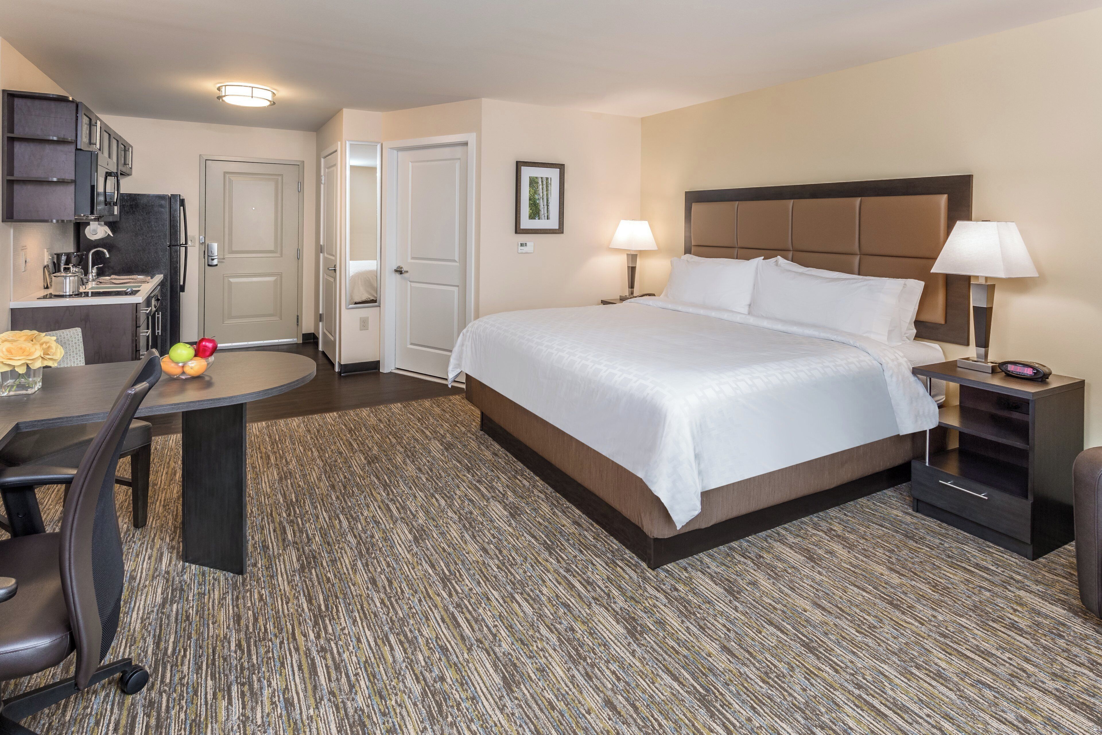 A hotel room with a bed, bedside tables, a desk, a chair, and a kitchenette.