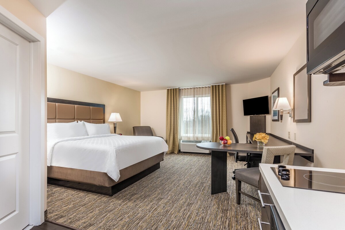 A hotel room with a bed, a desk, a chair, a television, and a window with curtains.