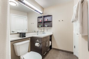 A modern bathroom with a toilet, sink, and mirror. There are shelves with toiletries and a towel rack. - Candlewood Suites Bensalem - Philadelphia Area by IHG (Feasterville-Trevose)