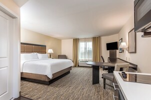 Quarto de hotel com uma cama, escrivaninha, cadeira, televisão e janela com cortinas.